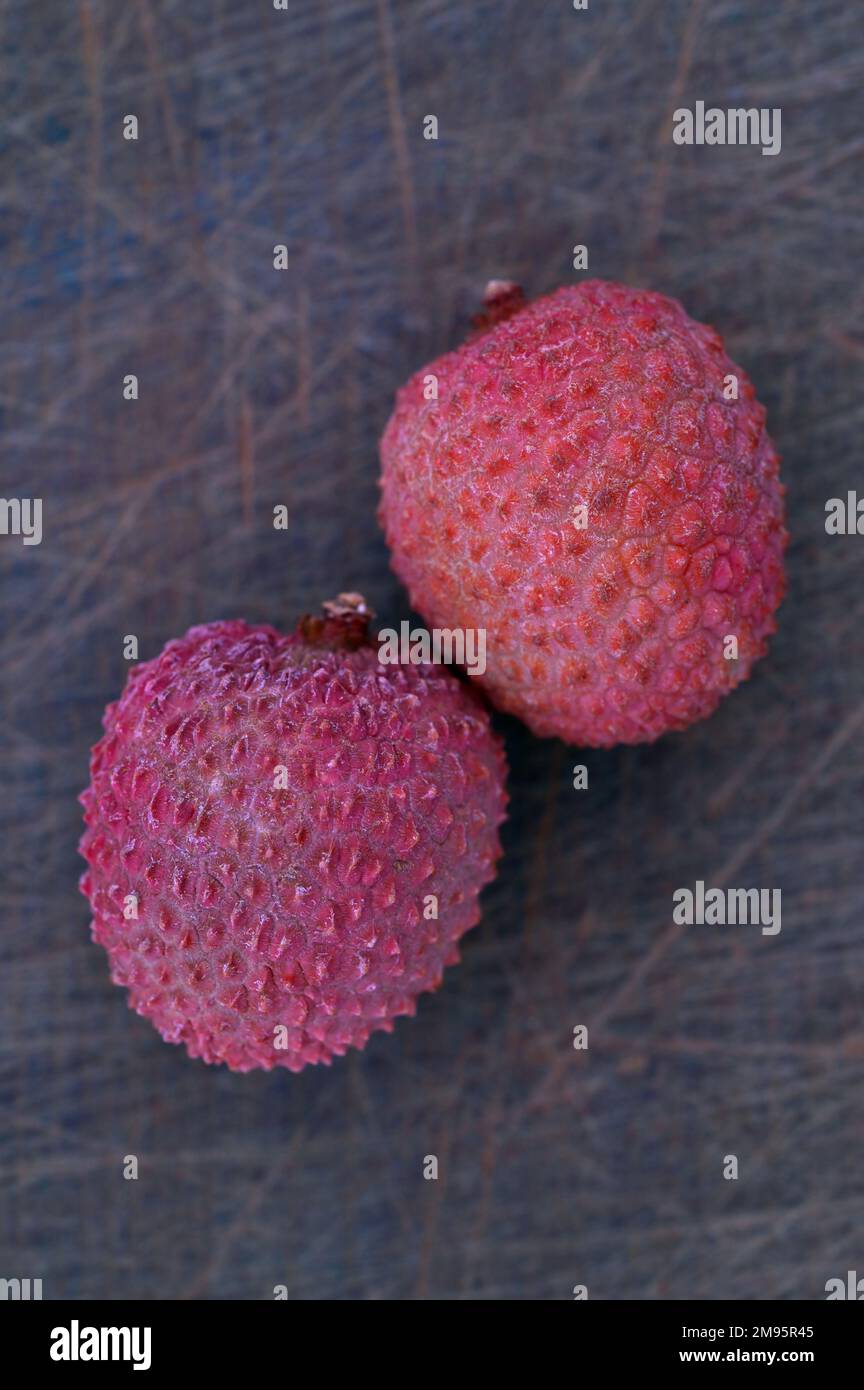 Zwei reife rosa Lychee-Früchte, die auf einem zerkratzten Schneidebrett liegen Stockfoto