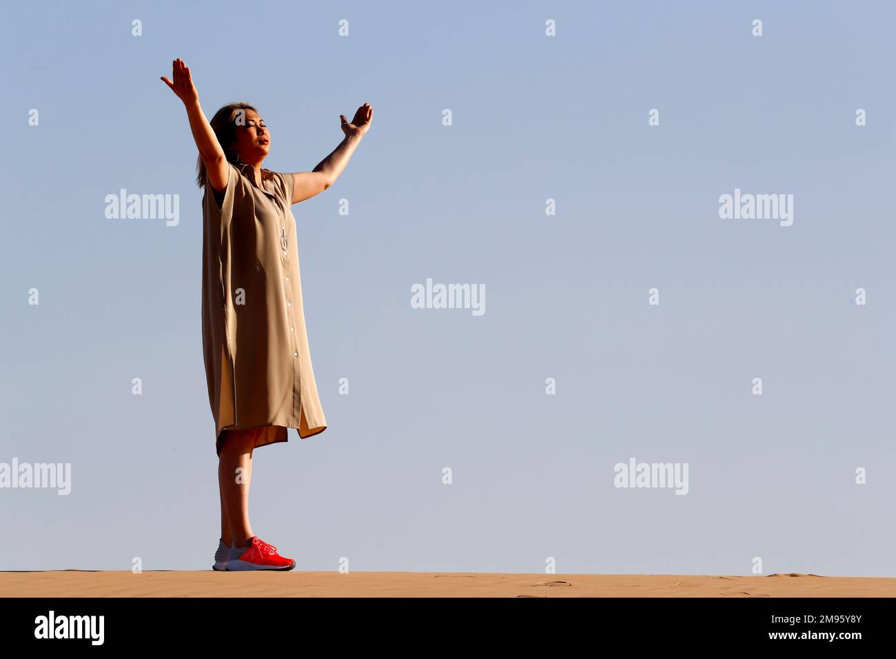 Eine Frau mit ausgestreckten Armen, die auf Sanddünen in der Wüste spaziert. Konzept für Religion, Glauben, Gebet und Spiritualität. Abu Dhabi. Vereinigte Arabische Emirate Stockfoto