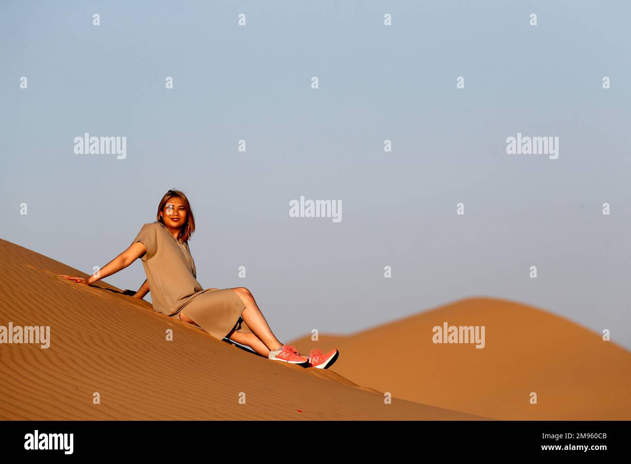 Eine Frau, die allein auf einer Sanddüne in Richtung der arabischen Wüste sitzt. Vereinigte Arabische Emirate. Stockfoto Eine Frau, die allein auf einer Sanddüne in Richtung der arabischen Wüste sitzt. Vereinigte Arabische Emirate. Stockfoto