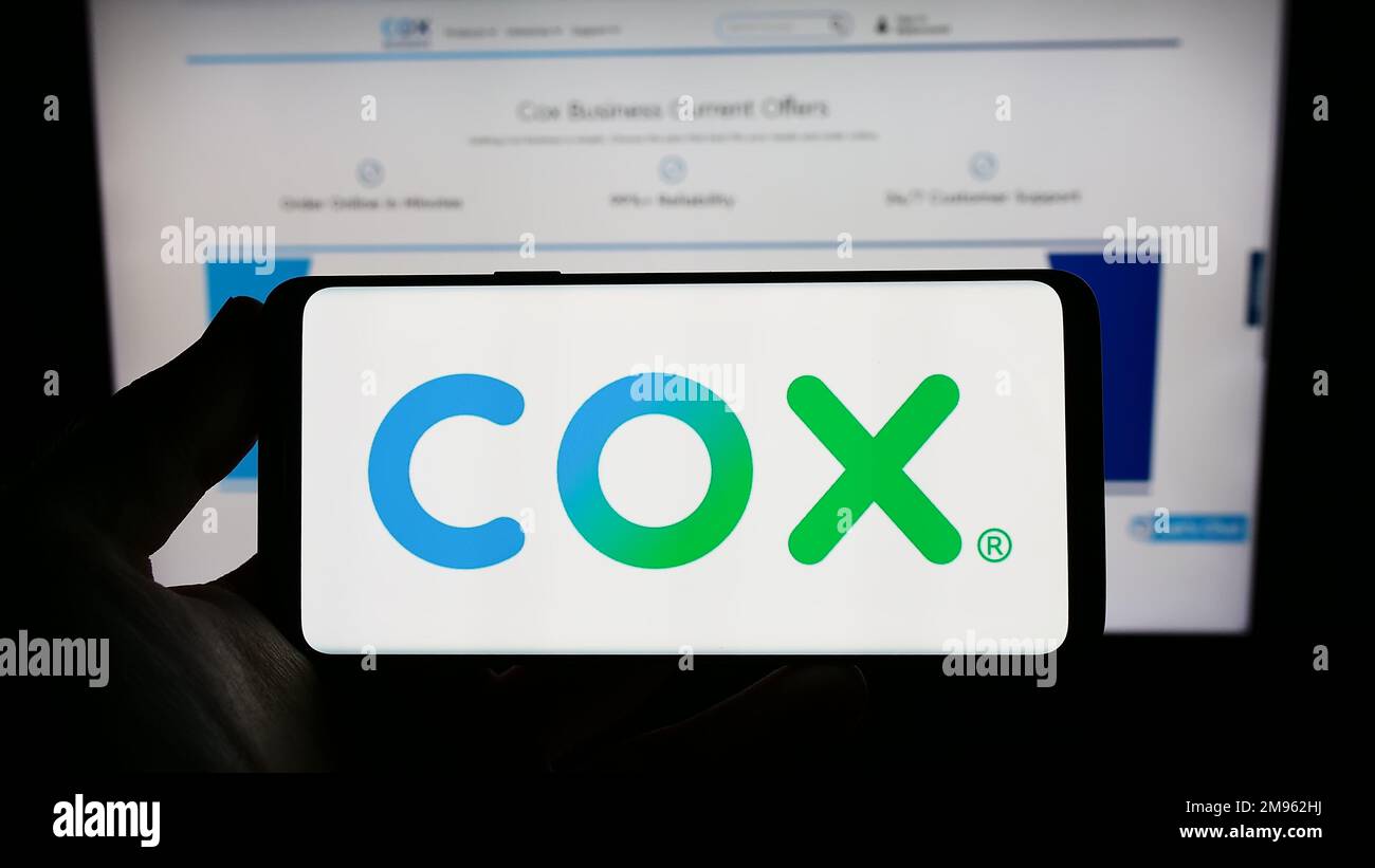 Person, die ein Smartphone mit dem Logo des US-Kabelfernsehunternehmens Cox Communications Inc. Auf dem Bildschirm vor der Website hält. Konzentrieren Sie sich auf das Display des Telefons. Stockfoto