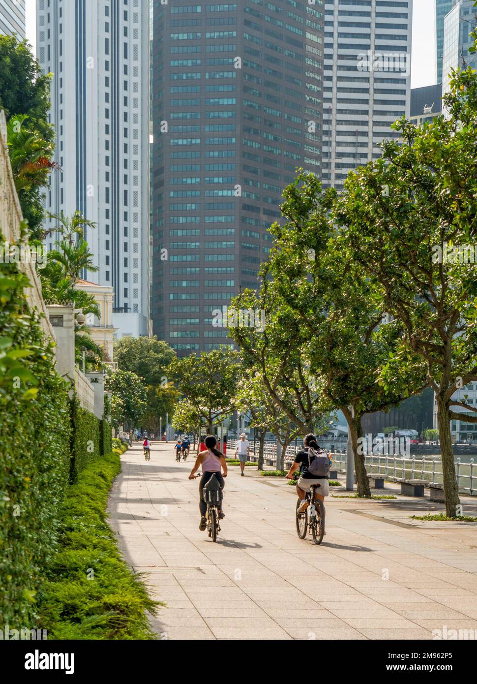 Zwei Radfahrerinnen fahren am Boat Quay Singapore entlang des Singapore River Stockfoto