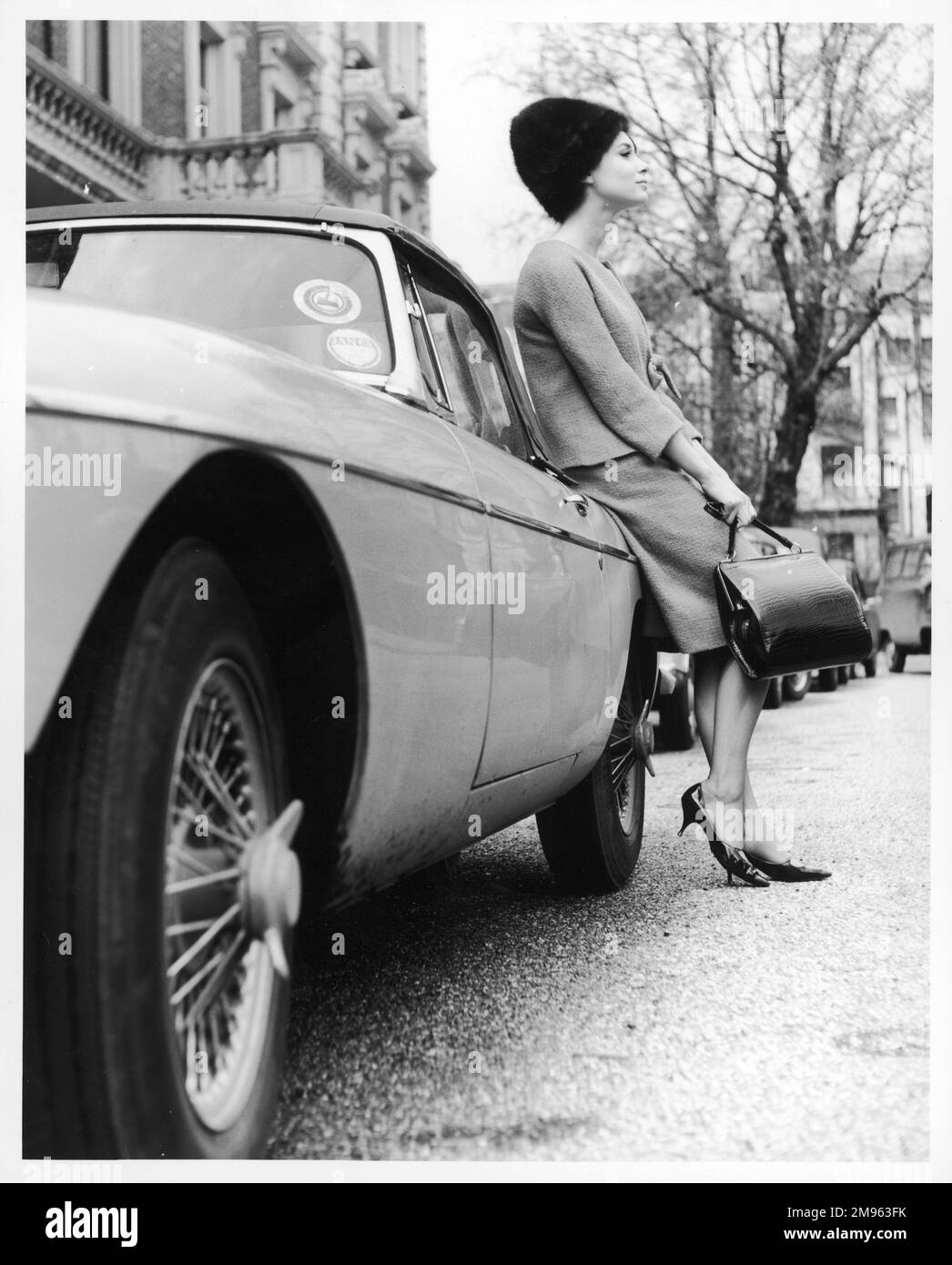 Ein ziemlich stilvolles Modell in einem Doppelanzug, Pelzmütze und passenden Stilettos und Handtasche, die sich gegen einen MG lehnen. Stockfoto