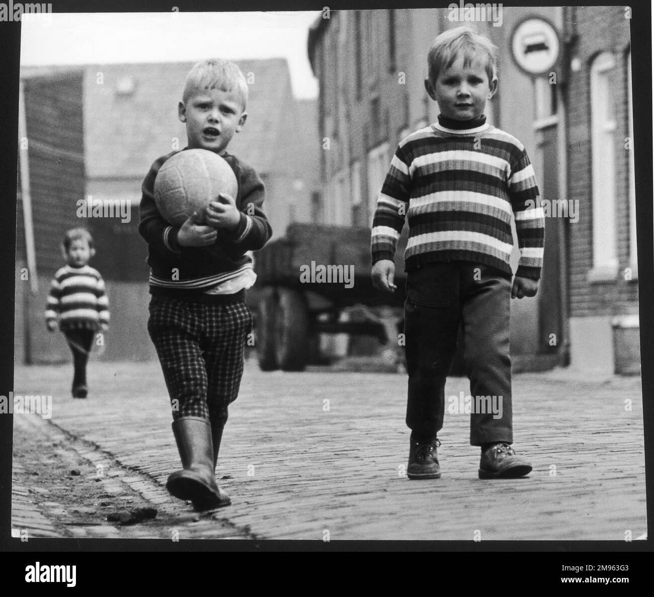 Zwei kleine Jungs, einer in einem gestreiften Pullover und der andere mit seinem Football. Stockfoto