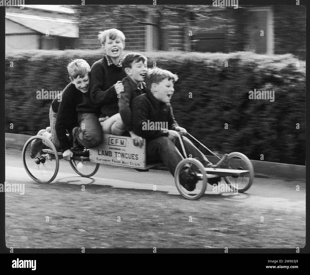 Vier Jungs auf einem selbstgemachten Go-Kart aus einer Kiste, die einst gefrorene Lammzungen enthielt, in Horley, Surrey. Zwei der Jungs gehören dem Fotografen und sie haben alle Spaß. Stockfoto
