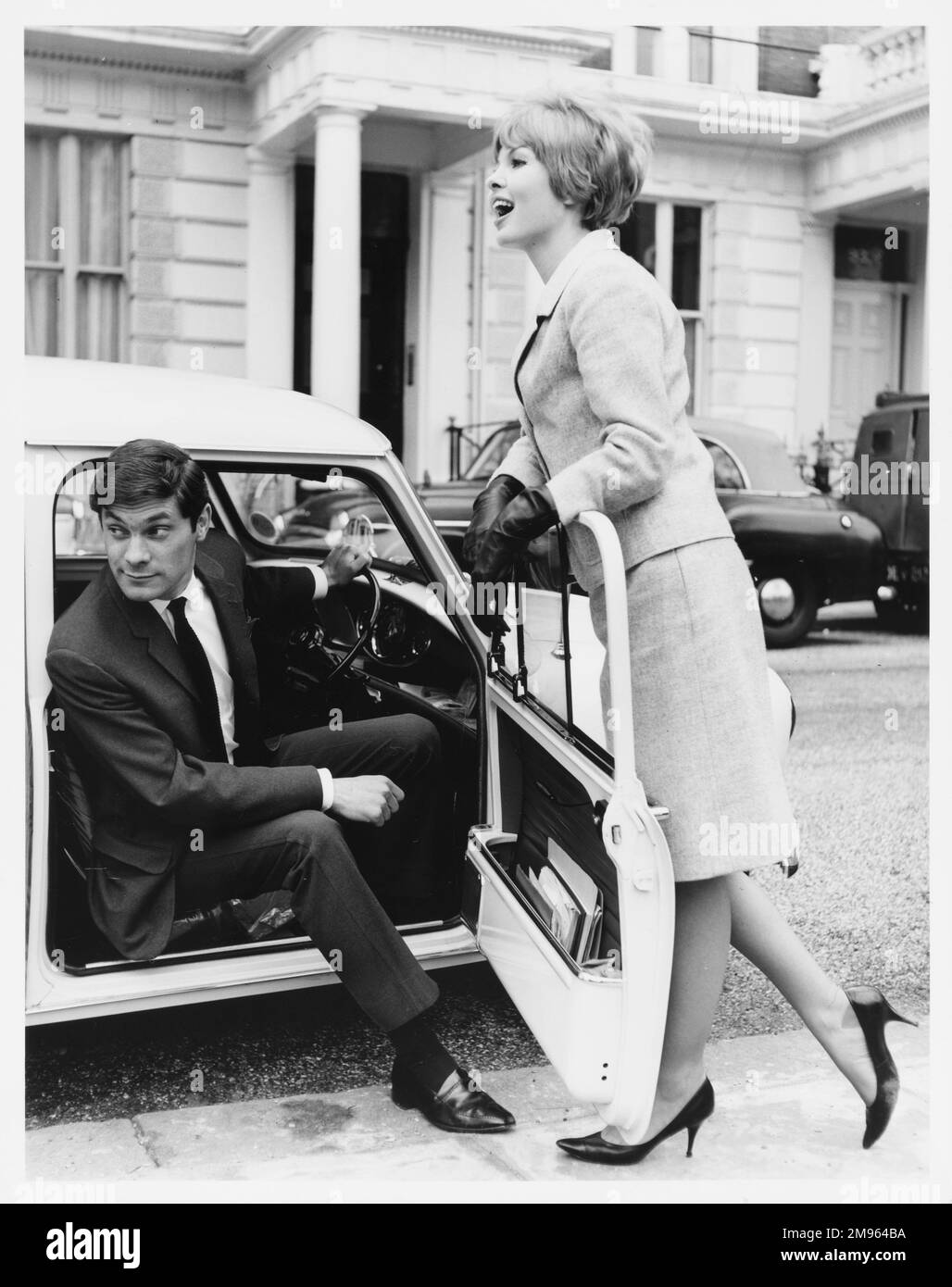 Ein Mann sitzt auf dem Fahrersitz eines Autos, während sich eine Frau an der offenen Tür lehnt. Stockfoto