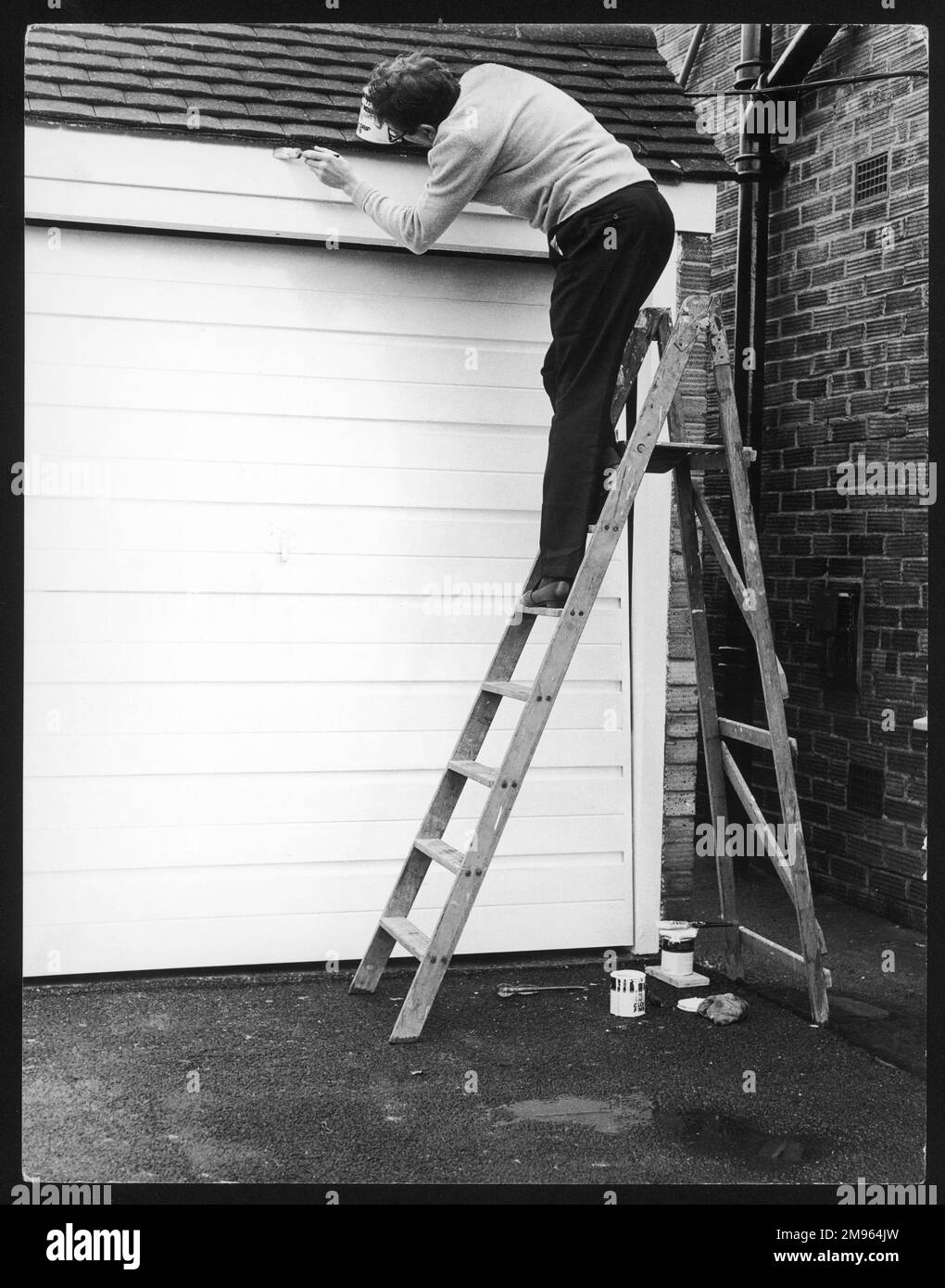 Ein Brite, der stolz auf das Haus ist, streicht die Tür und die Umgebung seiner Garage. Stockfoto