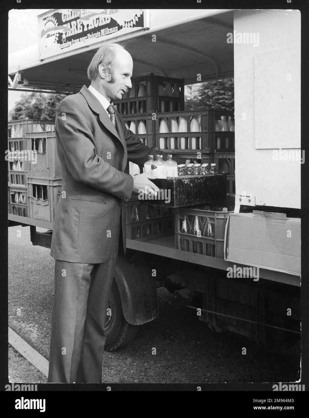 Ein (britischer) Regierungsinspektor, der die Qualität von Milchflaschen auf Kisten auf der Rückseite eines Milchfloßes überprüft. Stockfoto