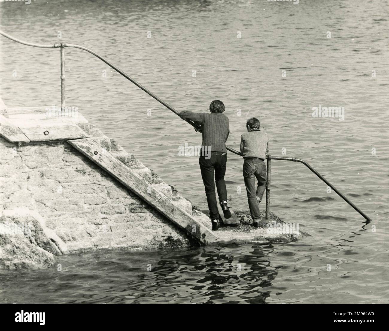 Zwei Jungen stehen direkt über dem Wasser, auf einigen Stufen, die hinunter zum Meer führen. Stockfoto