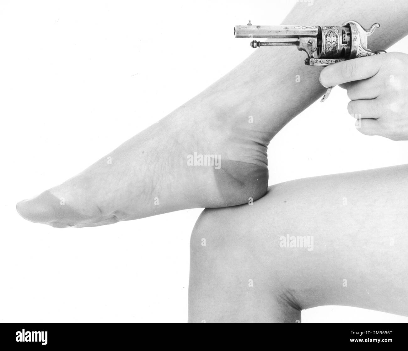 Eine Frau legt ihren Fuß auf ihr Knie und hält einen kleinen Revolver daneben. Stockfoto