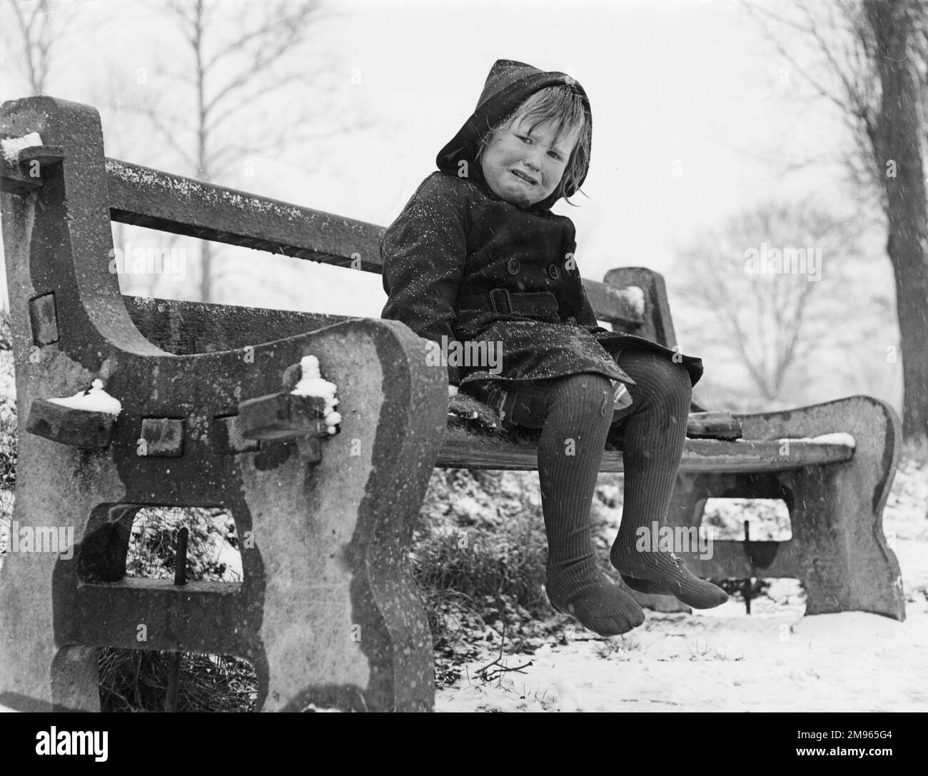 Ein kleines Mädchen, das auf einer Bank im Schnee sitzt und weint, weil sie eiskalte Zehen hat! Earlswood Lakes, Redhill Common, Surrey, England. Stockfoto