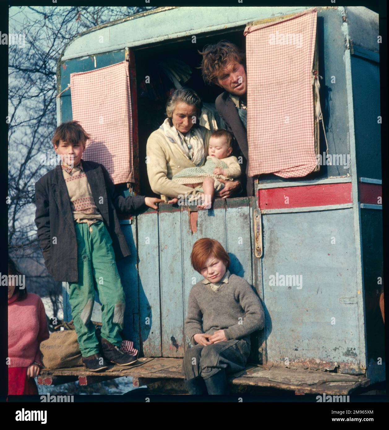 Drei Generationen einer Zigeunerfamilie stehen in, auf und um ihren Wohnwagen in dieser Winterszene in einem Reiselager Stockfoto