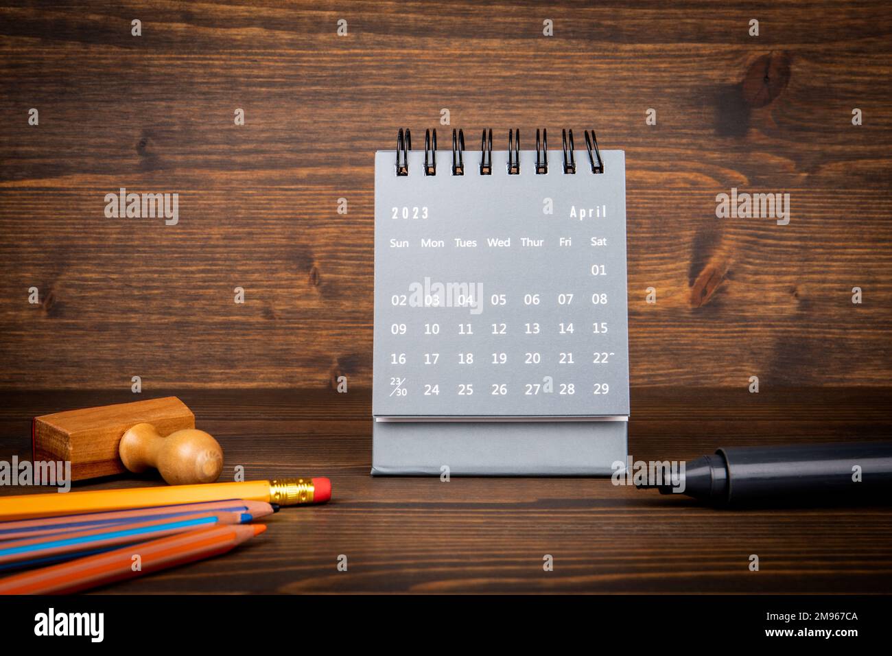 2023. April. Schreibtischkalender und Bürobedarf auf strukturiertem Holzhintergrund. Stockfoto