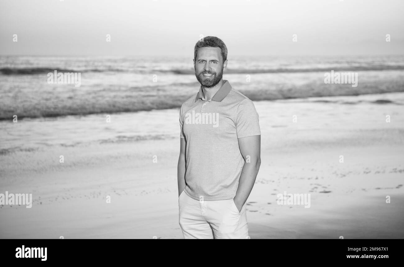 kaukasischer Kerl am Sonnenaufgangsstrand. Bärtiger Mann im Hemd. Sommermode-Stil. Sommerurlaub Stockfoto