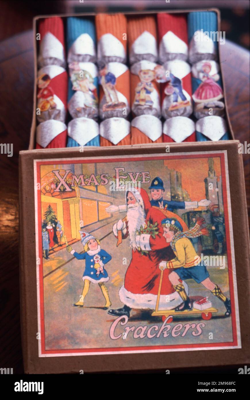 Eine schöne Schachtel mit weihnachtlichen Crackern aus den 1920er Jahren, mit intaktem Inhalt und dem Deckel mit einem hellen und fröhlichen Bild von Weihnachtsmann, der von einem Polizisten und zwei Kindern über die Straße geholfen wurde. Stockfoto