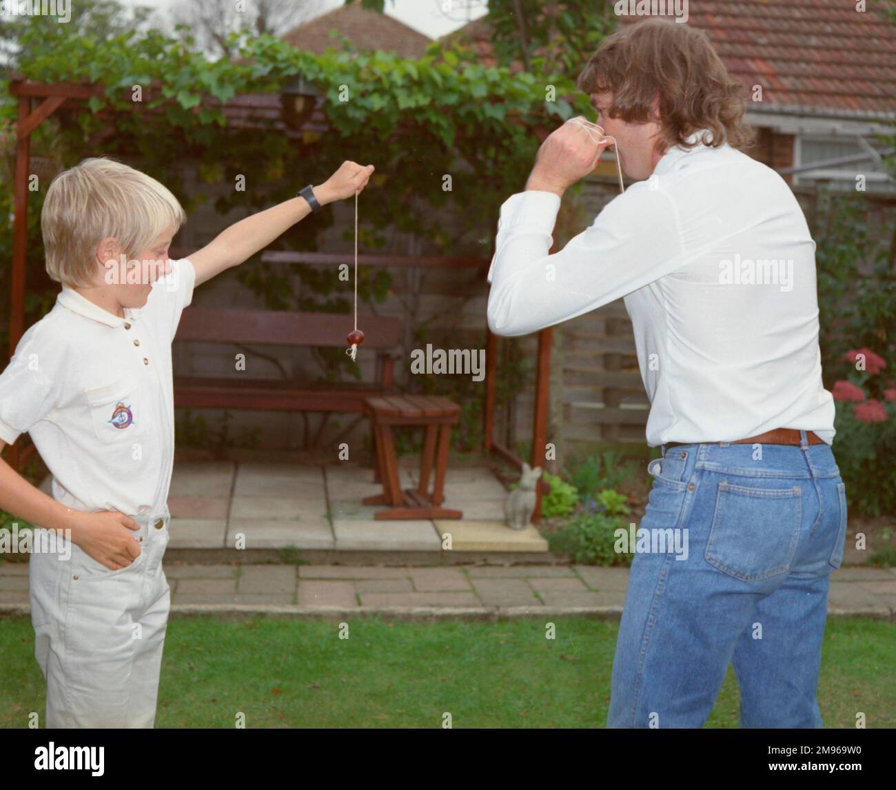 Ein Junge und ein junger Mann, die im Garten Conker spielen. Der Junge hält sein Konker fest, damit der Mann zuschlagen kann. Stockfoto