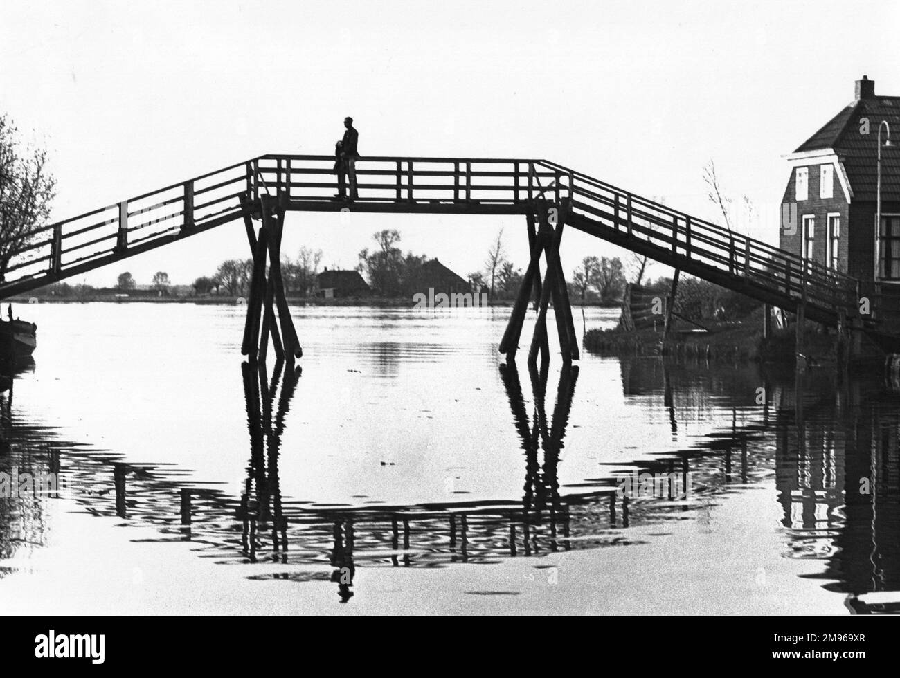 Eine Brücke in Silhouette über einen Wasserabschnitt, zusammen mit ihrer Reflexion. Stockfoto