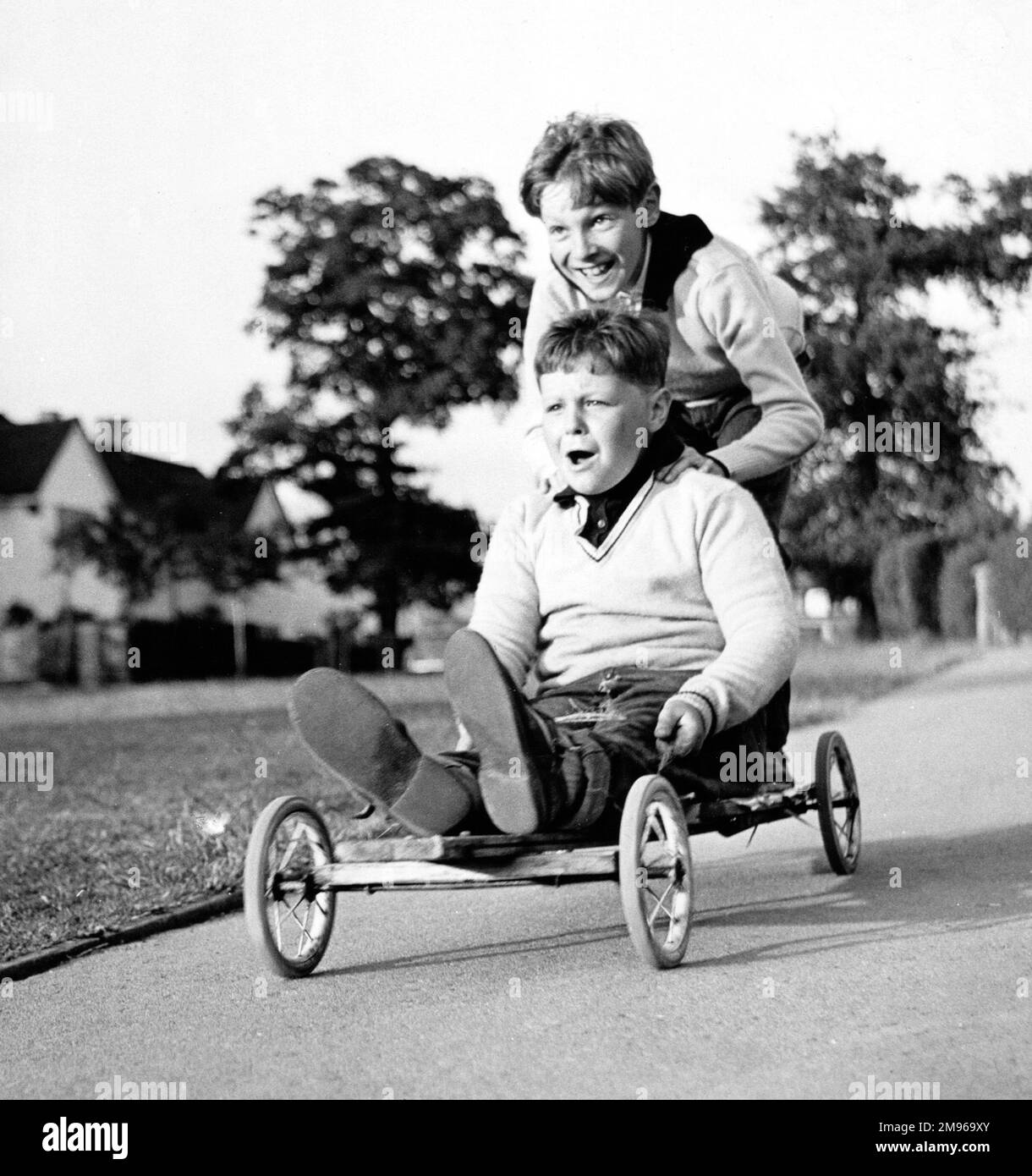 Zwei Jungs genießen eine Fahrt in einem hausgemachten Go-Kart in Horley, Surrey. Stockfoto