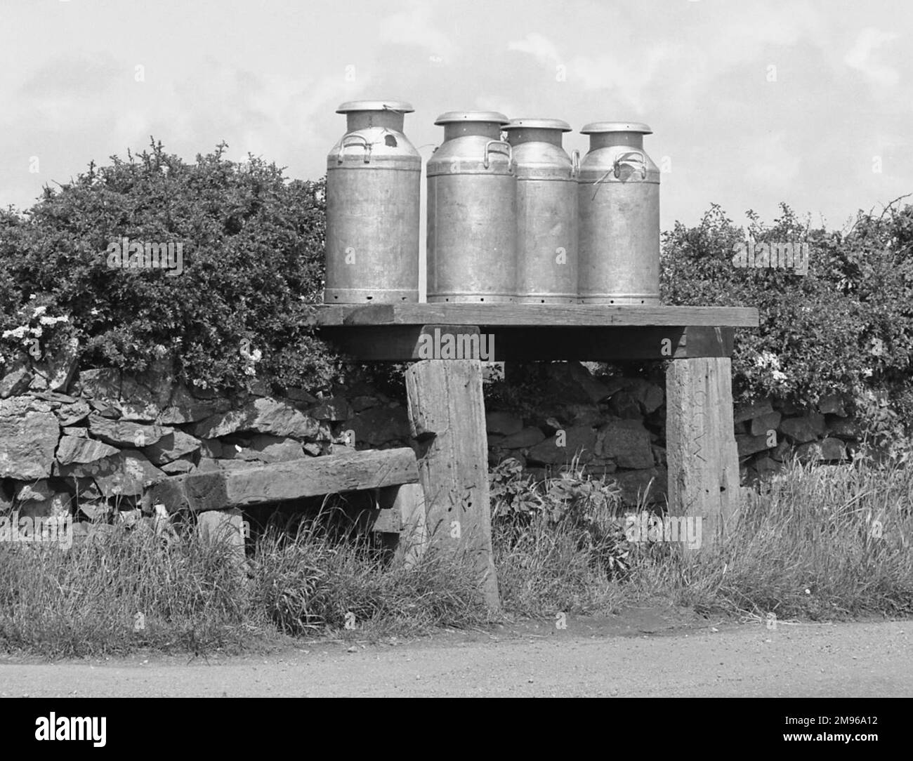 Vier Milchkannen auf einer Holzplattform am Rande einer Landstraße. Stockfoto