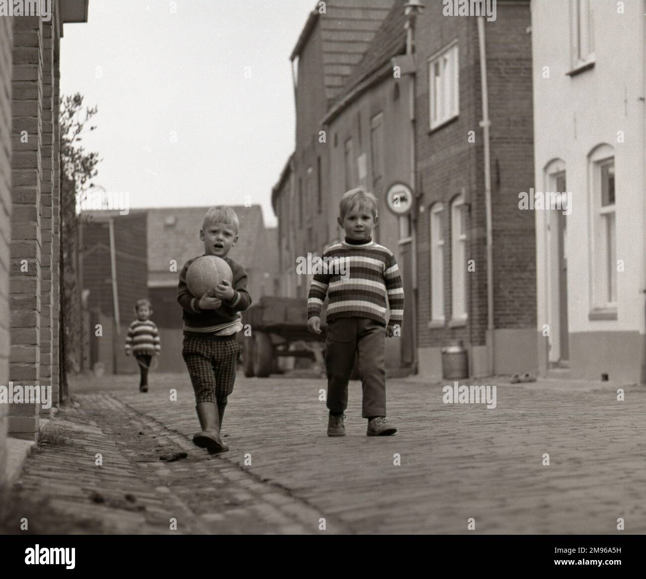Zwei kleine Jungs auf der Straße, einer in einem gestreiften Pullover und der andere mit seinem Football. Stockfoto