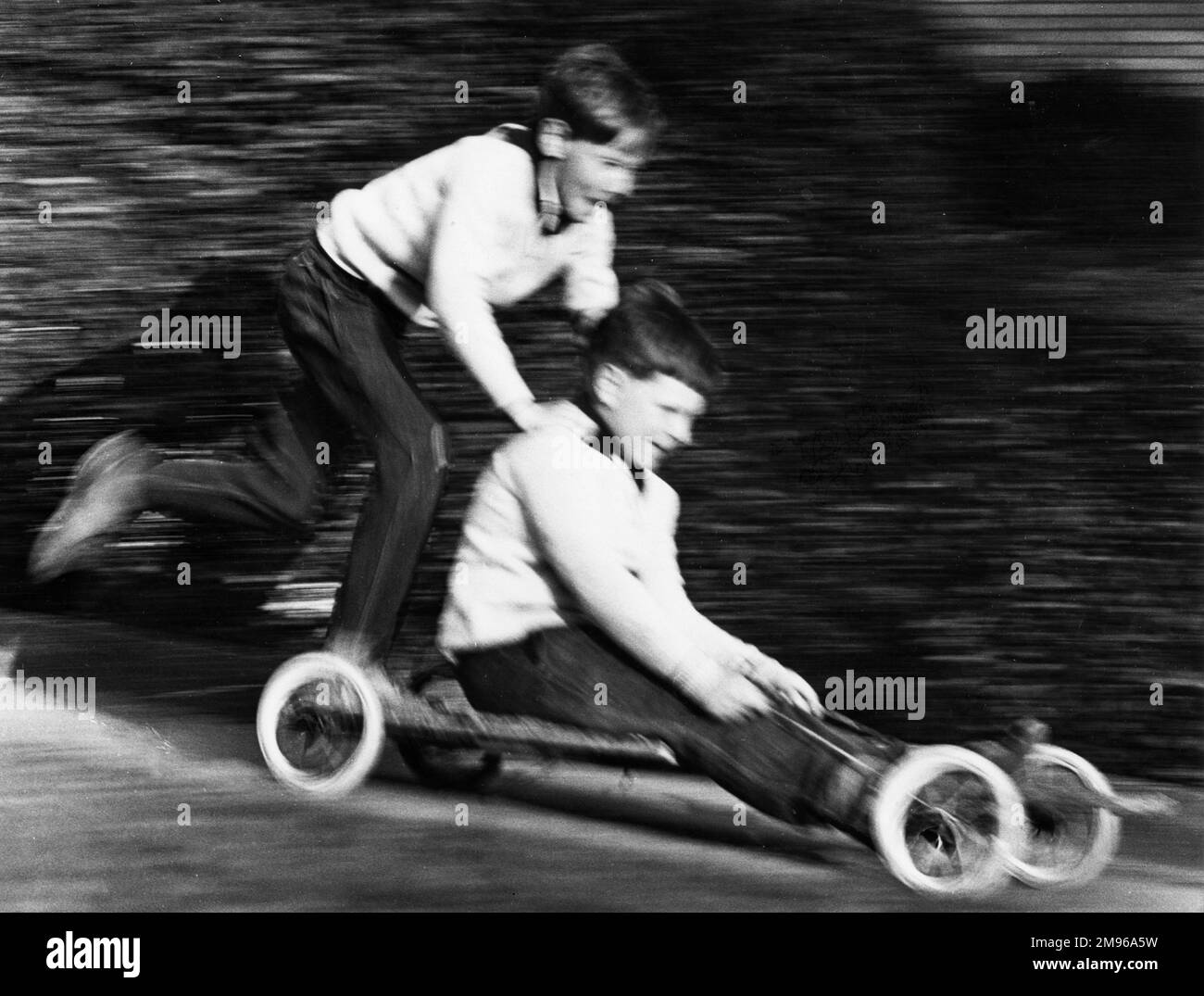 Zwei Jungs genießen eine Fahrt in einem hausgemachten Go-Kart in Horley, Surrey. Sie fahren so schnell, dass das Foto verschwommen ist! Stockfoto