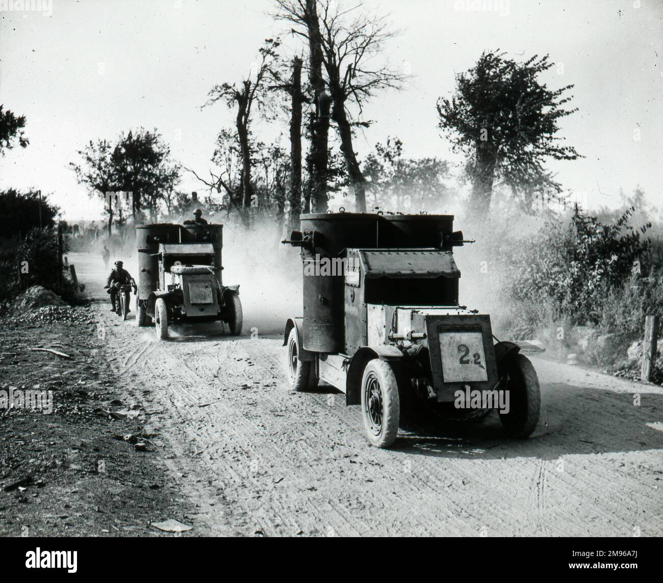 Zwei gepanzerte Autos und ein Motorradfahrer auf einer staubigen Landstraße im Ersten Weltkrieg. Stockfoto