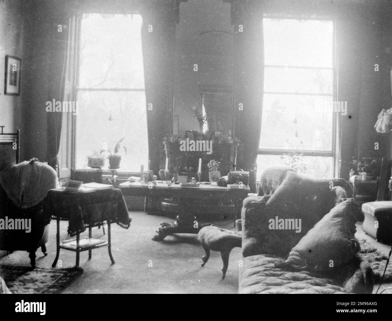 Der typische viktorianische Salon eines Landhauses, irgendwo in Südwales. Es gibt zwei große Schiebefenster mit einem Spiegel dazwischen, der eine Deckenrose reflektiert. Rechts ist eine Chaiselongue mit einem gepolsterten Stuhl. Stockfoto