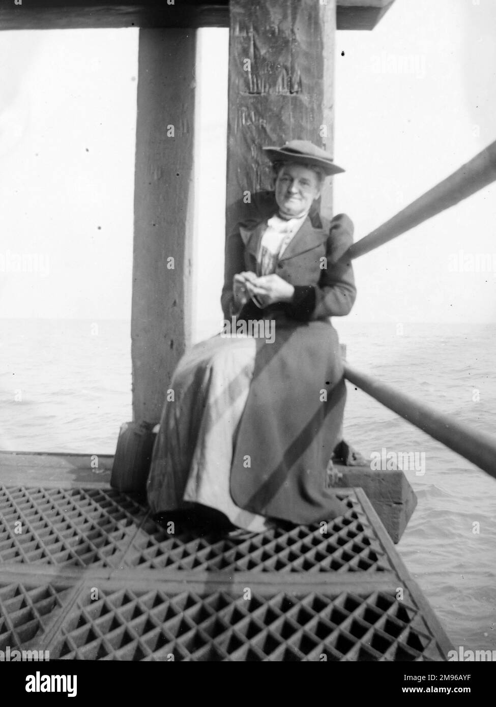 Eine Frau mittleren Alters, die in Fishguard, Pembrokeshire, Südwales auf das Fährboot wartet. Sie hat eine sonnige Ecke gefunden, in der sie sitzen kann, mit dem Meer hinter sich. Stockfoto