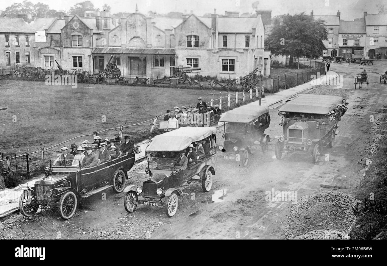 Ein Greens Motors Charabanc-Ausflug mit insgesamt fünf Charabancs führt durch die Straßen von Haverfordwest, Pembrokeshire, South Wales. An diesem Punkt der Reise sind sie genau gegenüber den Limousinen -- Stapel von Kalk sind am Straßenrand auf der rechten Seite zu sehen. Im Hintergrund befindet sich die Bohrhalle, in der deutsche Waffen aus dem Ersten Weltkrieg deutlich sichtbar sind. Stockfoto