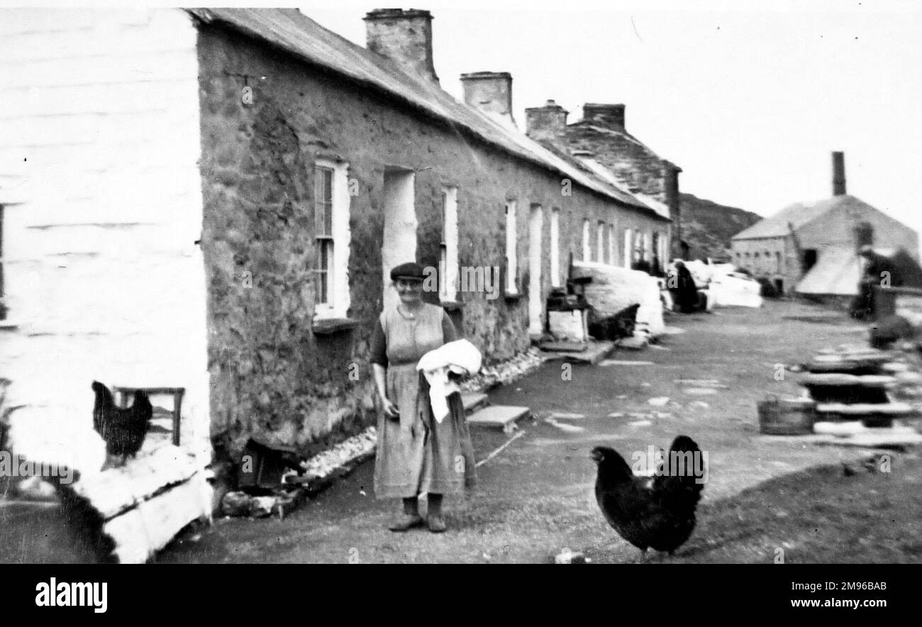 Eine Straßenszene im Küstendorf Porthgain, Pembrokeshire, Südwales. Eine Frau mittleren Alters steht und lächelt vor der Kamera. Stockfoto