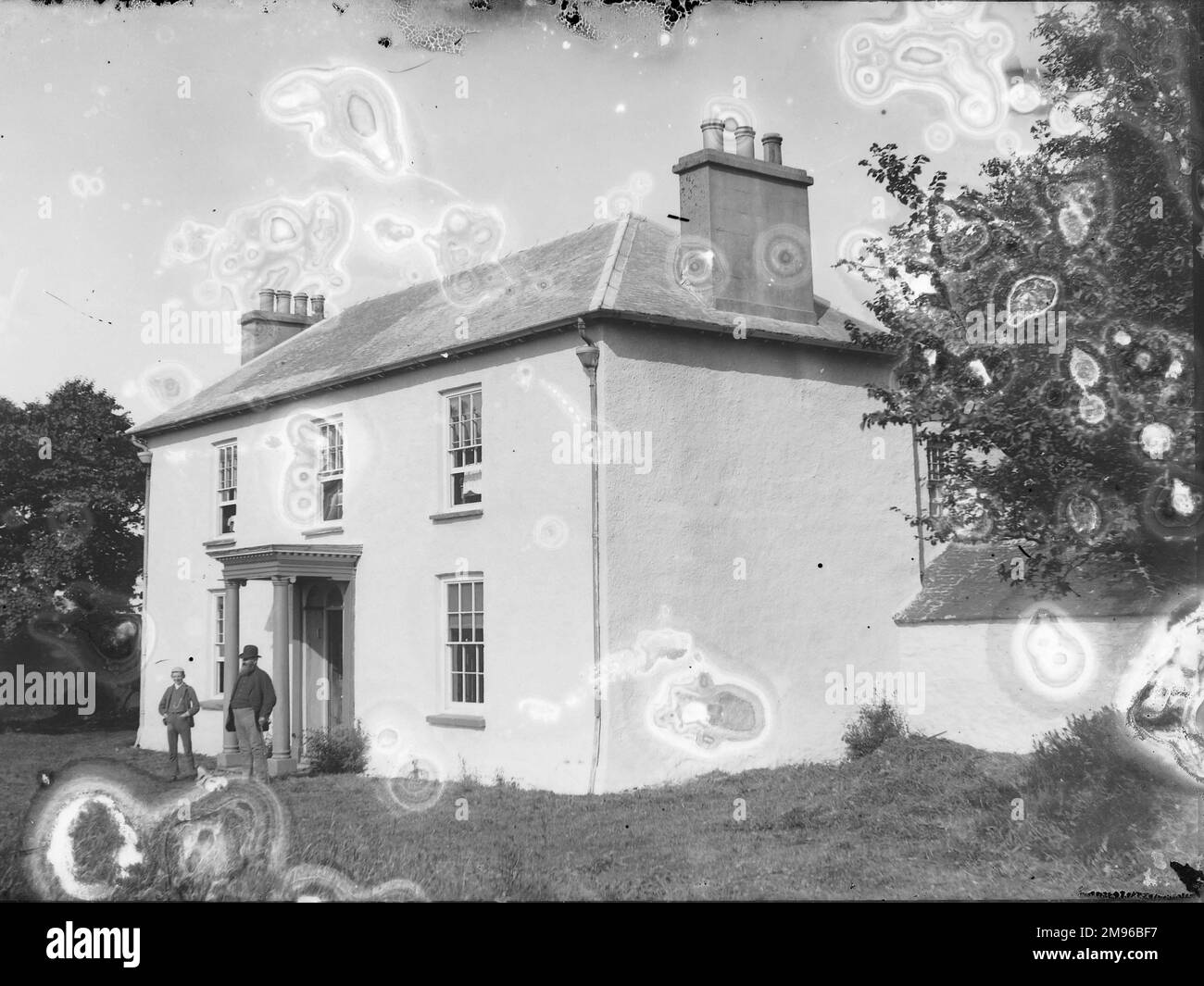 Ein weiß getünchtes georgianisches Haus in Mid oder South Wales, mit einem dicken Mann und einem dünnen Jungen, der vor dem Eingang steht. Stockfoto