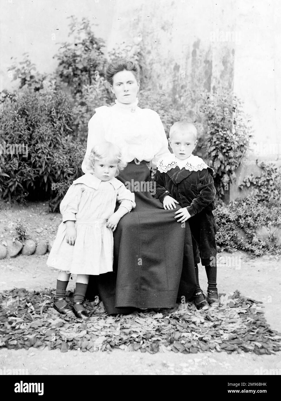 Eine Mutter und ihre beiden Kinder posieren für ihr Foto in einem Garten, wahrscheinlich irgendwo in Mid Wales. Der kleine Junge trägt einen Samtanzug mit kunstvollem Spitzenkragen. Das kleine Mädchen trägt schlichtere Kleidung. Stockfoto