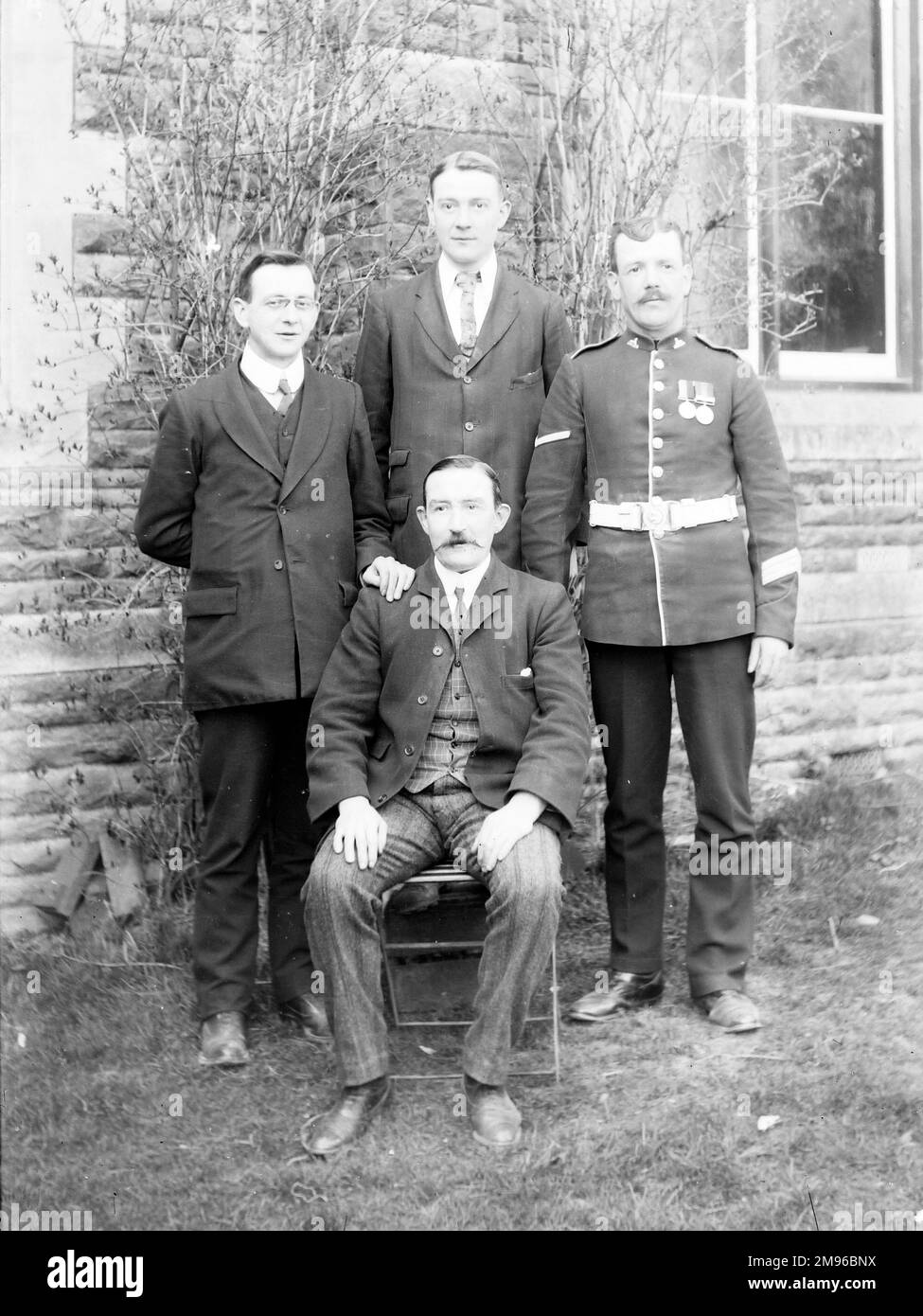 Ein Familienfoto in einem Garten, mit einem Vater und seinen drei Söhnen, einer davon in Uniform, während des Ersten Weltkriegs. Stockfoto