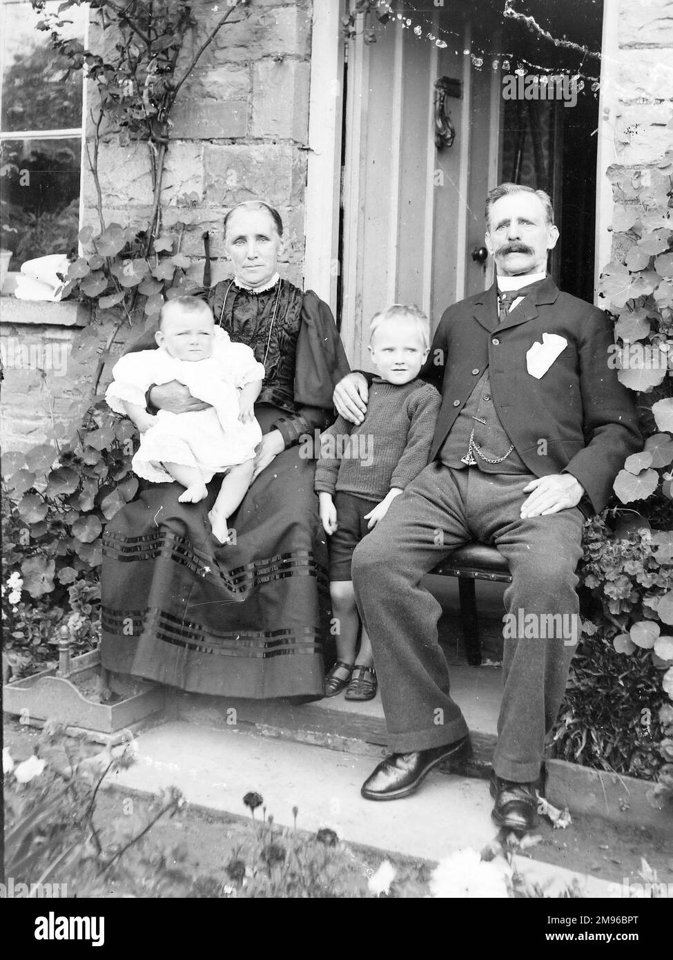 Stolze Großeltern, die in ihrem Haus sitzen, mit zwei Kindern, einem Baby und einem kleinen Jungen. Stockfoto