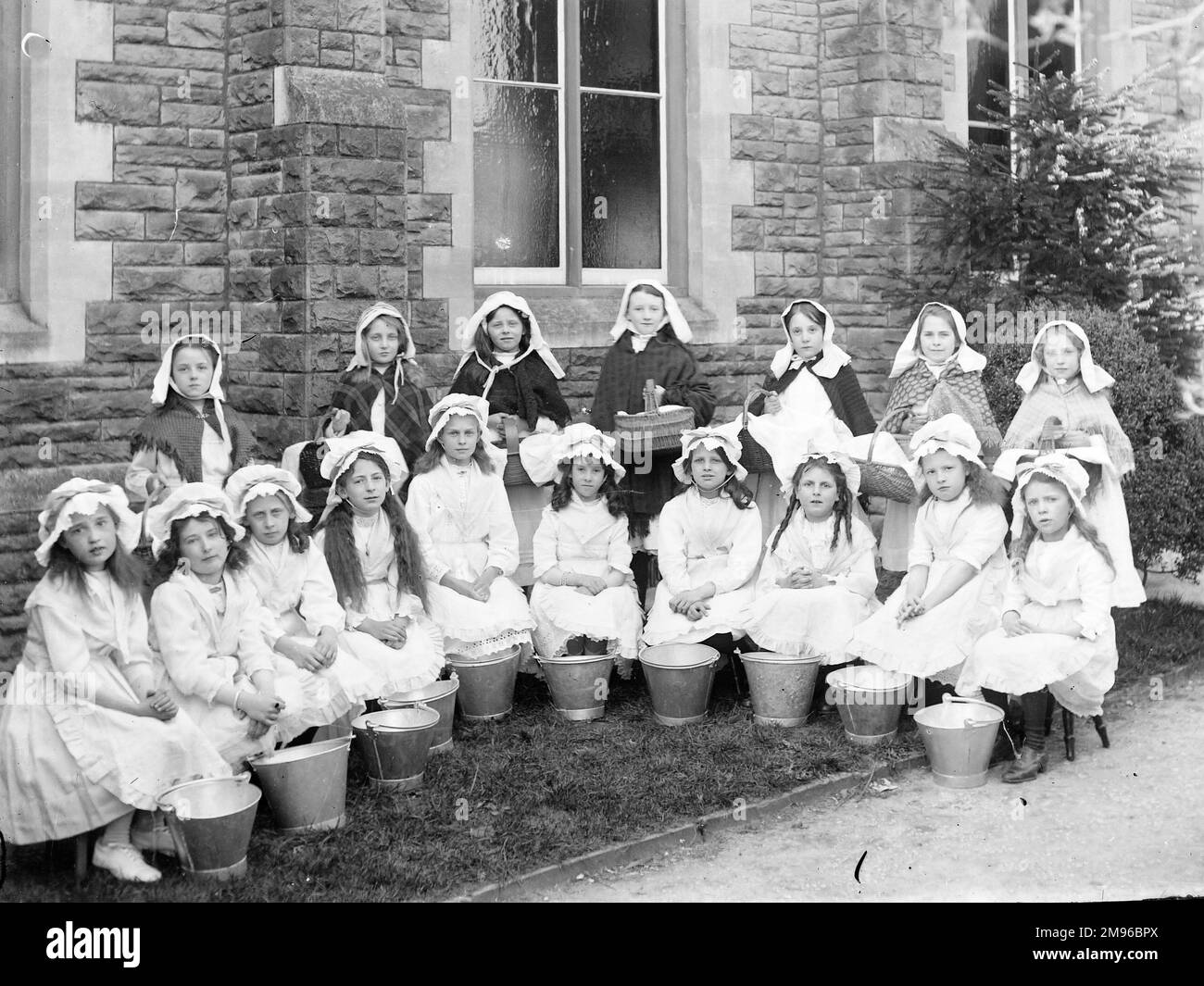 Eine Gruppe edwardianischer Schulkinder, gekleidet als Milchmädchen, mit Körben und Eimern. Das Gebäude im Hintergrund ist möglicherweise das Old Rectory im Dorf Llangattock, nahe Crickhowell, Powys, Mid Wales. Stockfoto