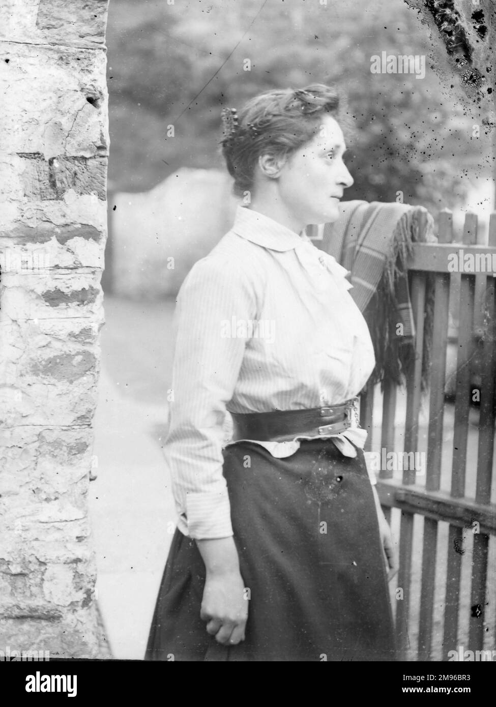 Eine Frau im Profil, die an einem Tor steht, Mid Wales, mit einem durchdachten Gesichtsausdruck. Eine gemusterte Decke oder ein gemusterter Schal ist oben über dem Tor angebracht. Stockfoto