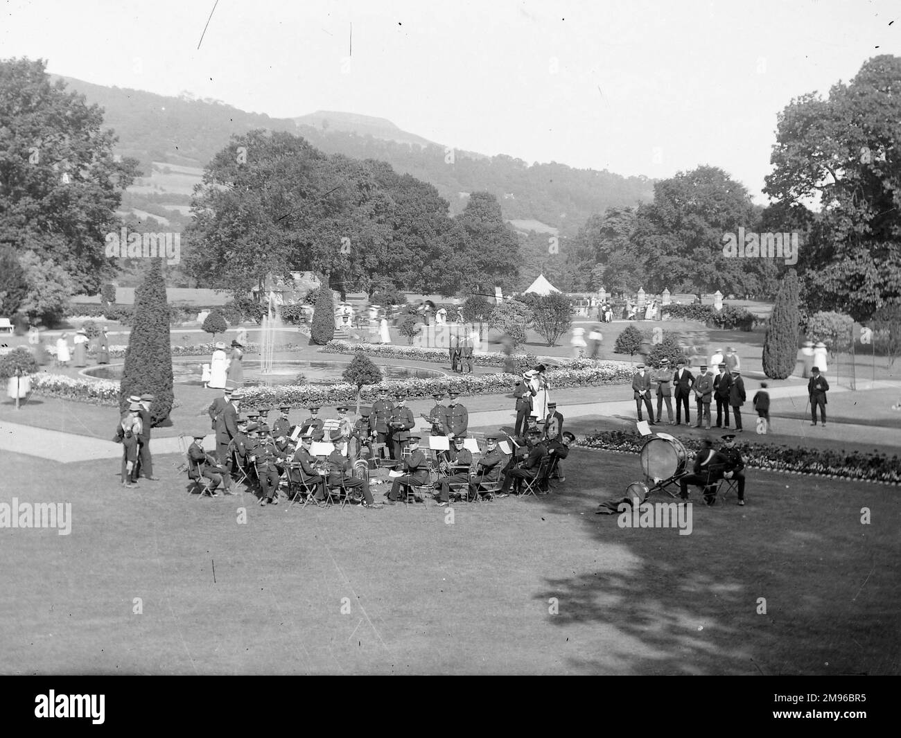 Eine Militärkapelle auf dem Gelände eines großen Landhauses in Crickhowell, Powys, Mid Wales. Verschiedene Zivilisten laufen herum und genießen die Gärten und den Brunnen. Stockfoto