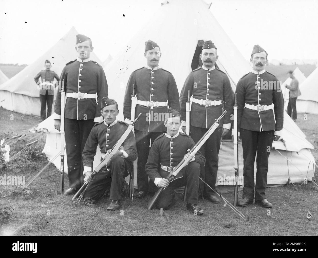 Eine Gruppe von vier Soldaten und zwei Kadetten in einem Trainingslager, die vor einem Zelt für ihr Foto posieren. Sie sind alle in Uniform und haben Gewehre in der Hand. Stockfoto