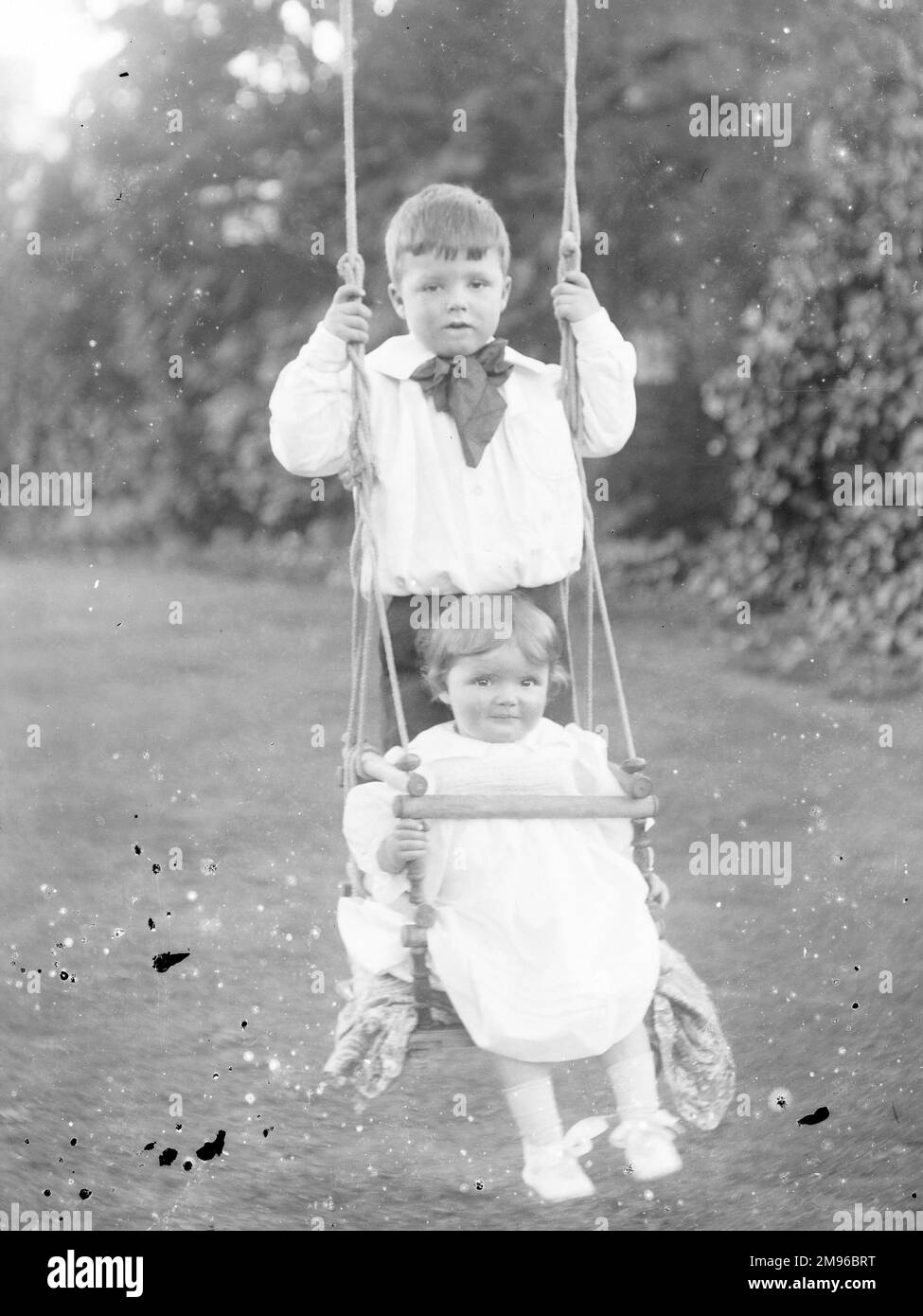 Zwei edwardianische Kinder auf einer Schaukel in einem Garten, Mid Wales. Die Schaukel verfügt vorn über einen Sicherheitsbügel. Stockfoto