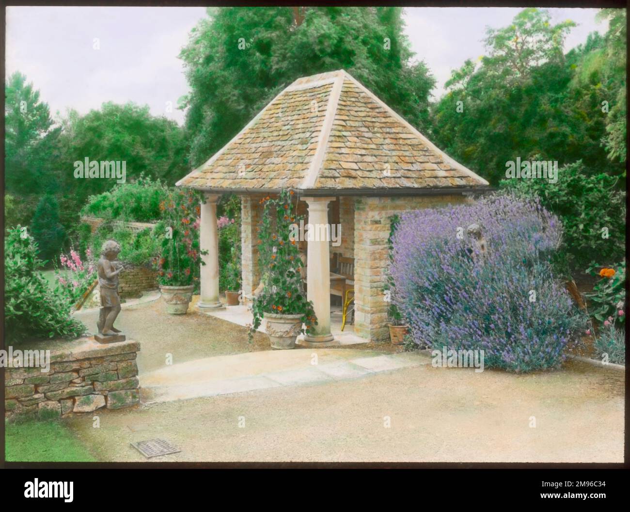 Ein Gartensitz in den formellen Gärten von Abbotswood, Stow on the Wold, Gloucestershire. Der Sitz hat zwei Säulen im klassischen Stil (Toskana) an der Vorderseite und ein gefliestes Dach. Die Gärten wurden von Sir Edwin Lutyens geschaffen. Stockfoto