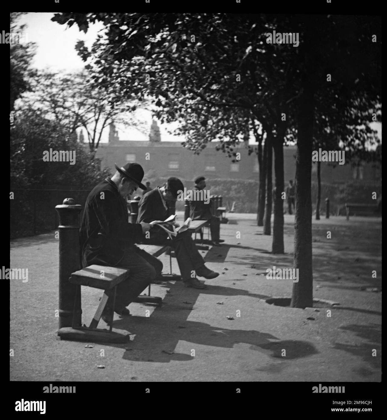 Männer, die auf Bänken in einem nicht identifizierten Londoner Park sitzen. Im Hintergrund ist eine Terrasse mit Häusern zu sehen. Stockfoto