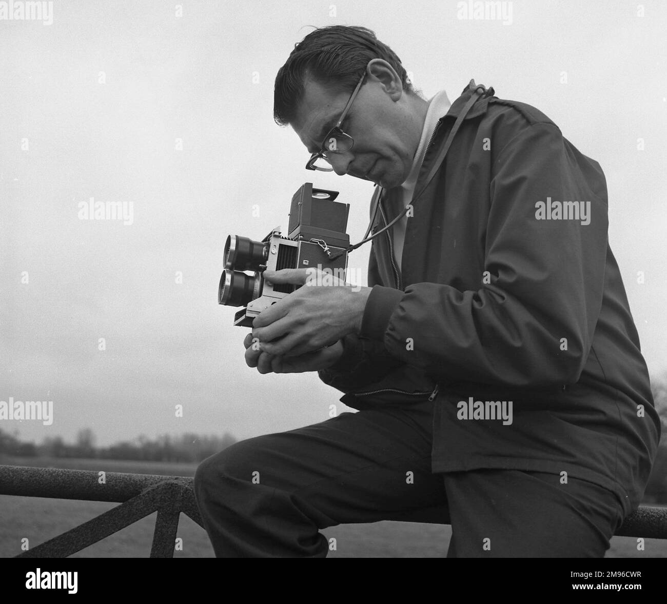 Ein Fotograf sitzt auf einem Zaun und schaut durch den Sucher seiner Kamera. Stockfoto