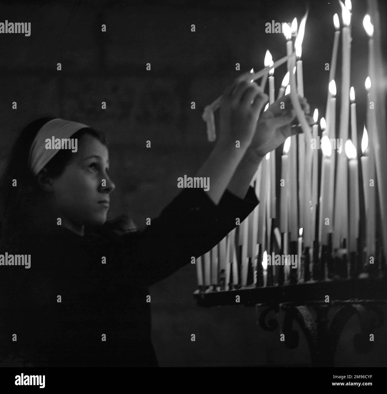 Eine junge Frau in einer Kirche zündet eine Kerze an. Stockfoto