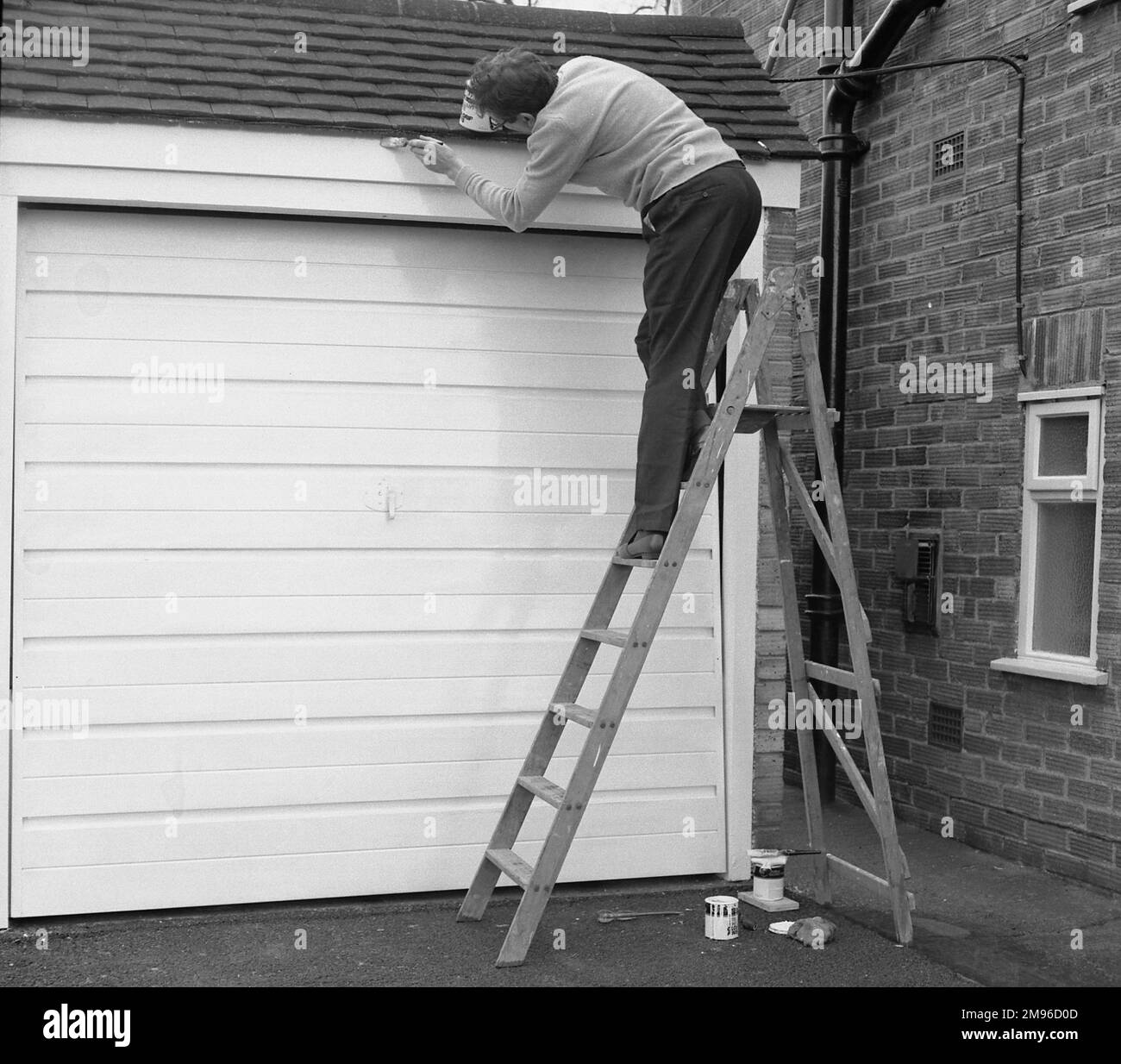 Ein britischer Hauseigentümer kletterte eine Leiter hoch, streichelte die Tür und die Umgebung seiner Garage. Stockfoto