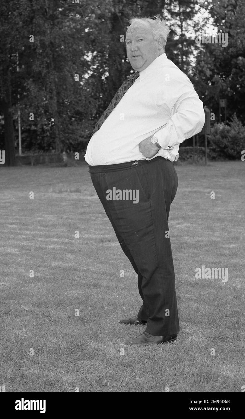 Ein ziemlich dicker Mann steht in einem Feld in Hemd und Hose und schaut kompromisslos in die Kamera. Stockfoto