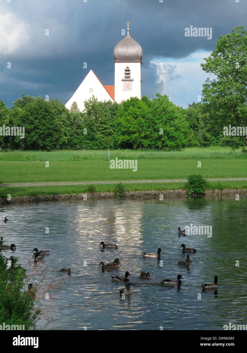 Blick auf die Leiden-Christi-Kirche in München. Es liegt in einer Parklandschaft mit einem Teich im Vordergrund. Stockfoto