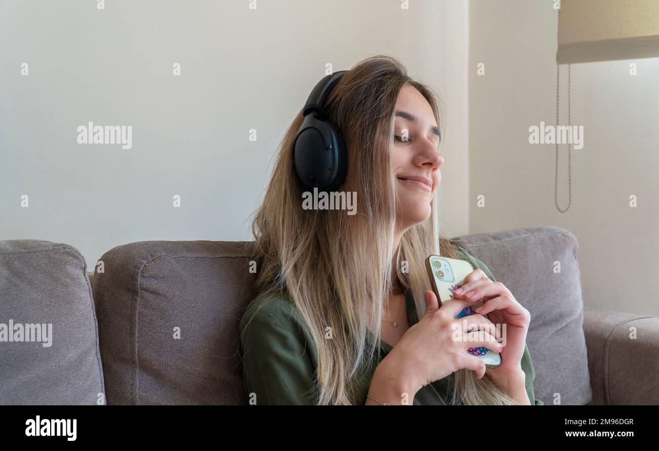 Angenehme Frau, die zu Hause Musik hört. Glückliche junge Frau, die fröhliche Musik hört und lächelt. Stockfoto