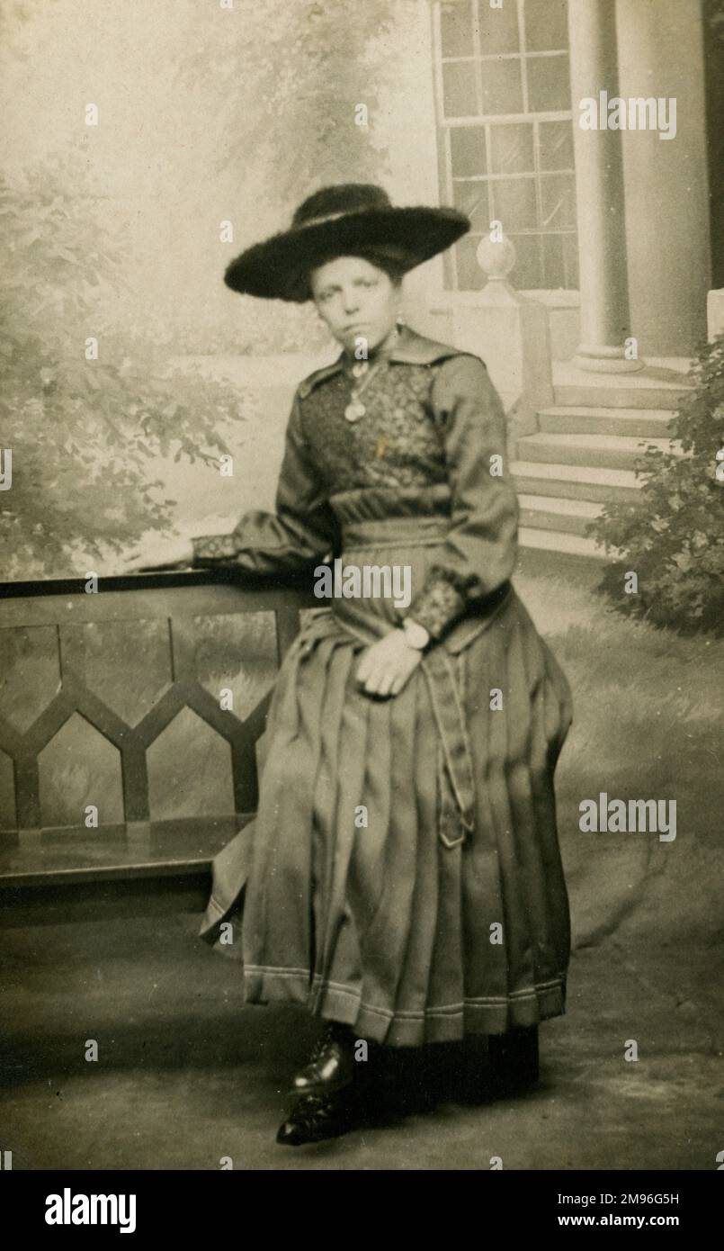 Eine Frau mit großem Hut und Faltenrock posiert auf einer Bank in einem Fotostudio Stockfoto