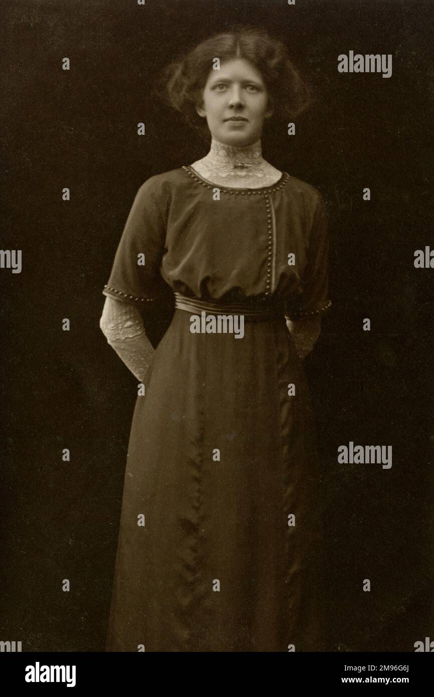 Eine Frau aus dem frühen 20. Jahrhundert trägt ein langes Kleid, an der Taille gereiht, die Hände hinter dem Rücken gehalten. Stockfoto