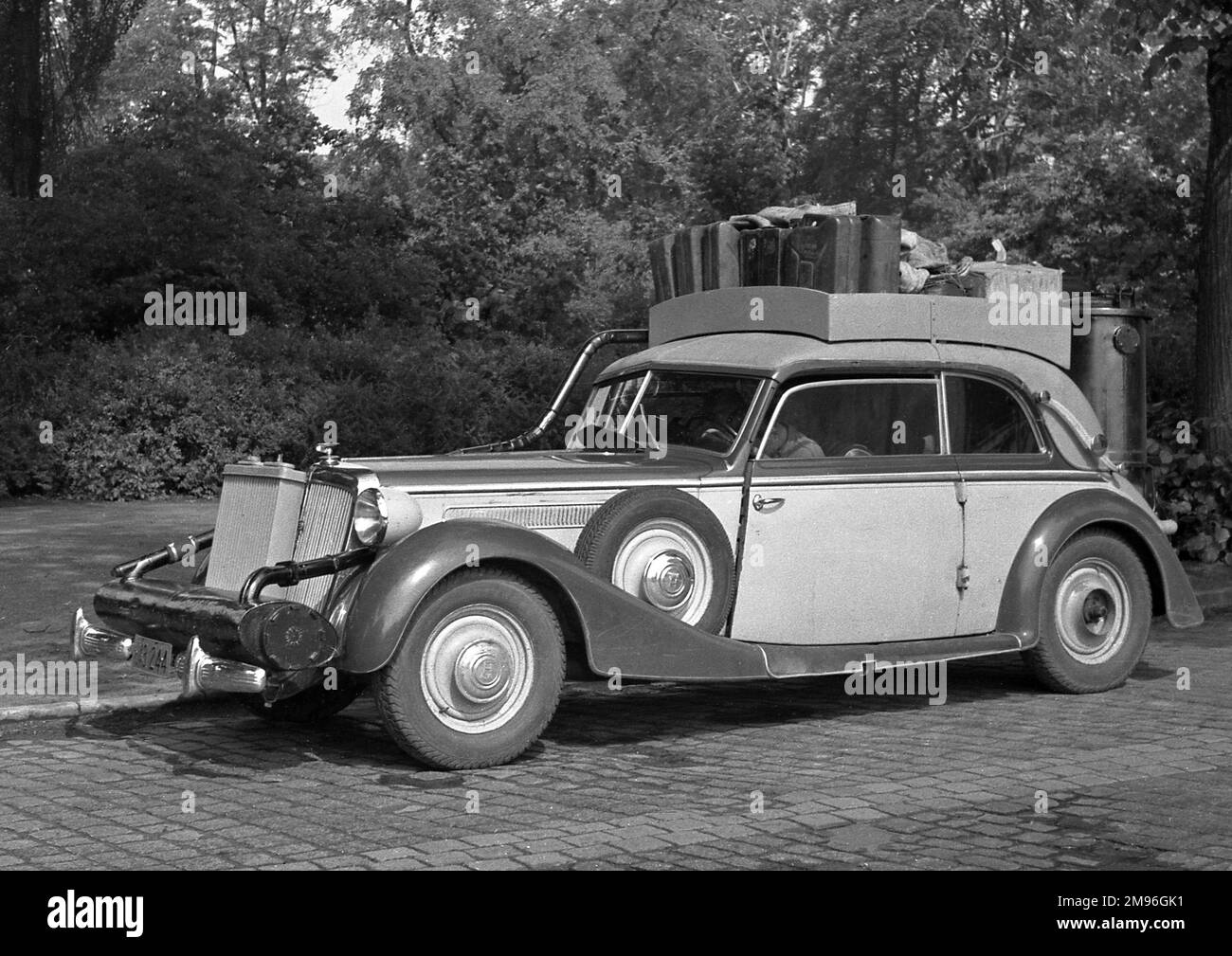 Ein Auto mit mehreren Koffern, die auf dem Dachgepäckträger zusammengepackt sind. Beachten Sie, dass das Stromversorgungssystem des Holzgasgenerators – Deutschland, 1945 – aufgrund der schweren Benzinknappheit Ende WW2 unerlässlich ist. Stockfoto