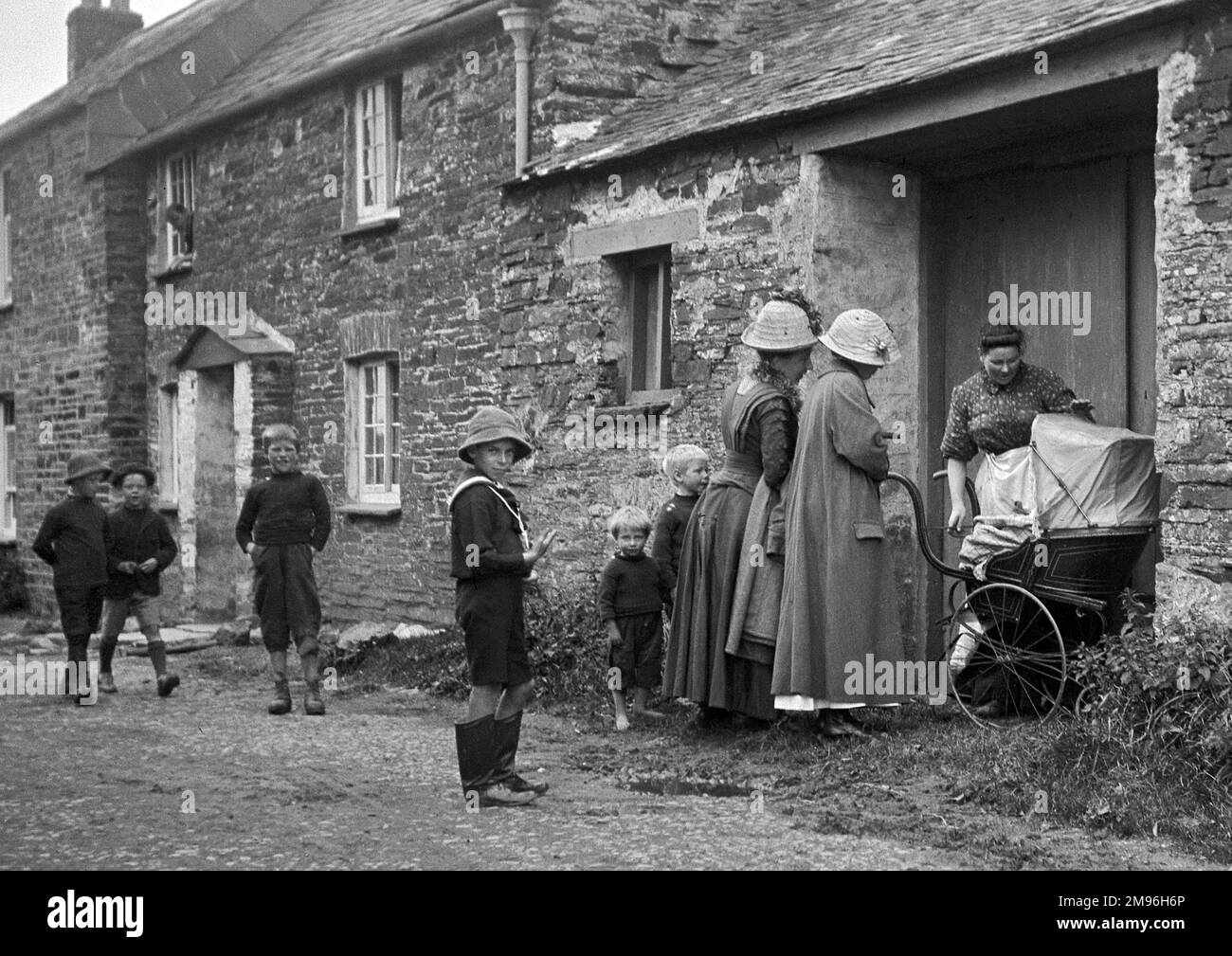 Szene in einer Dorfstraße, mit Frauen um einen Kinderwagen versammelt, und Jungen spielen. Stockfoto